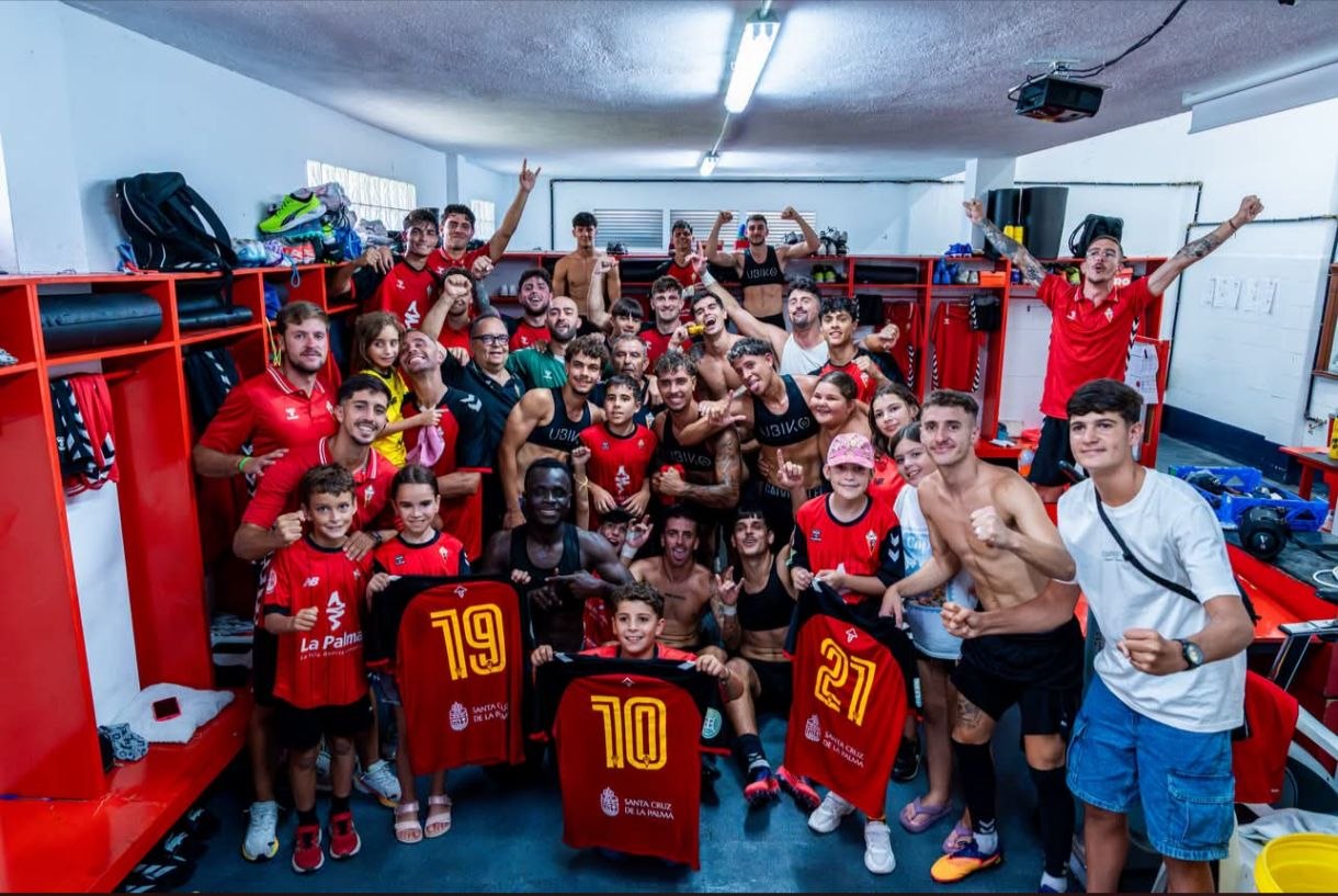 Plantilla, cuerpo técnico y jóvenes aficionados del CD Mensajero celebrando la victoria en el vestuario